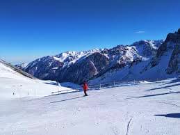 Skier on snowy slope with snow-covered mountain range and valley in background under clear blue sky